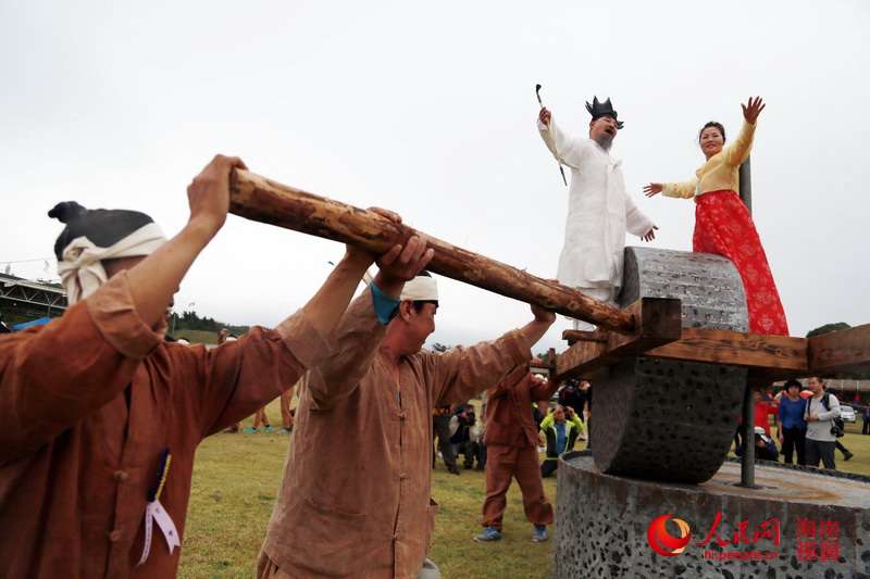 民俗節(jié)上，兩名身著華麗服裝的人站在“石磨”上載歌載舞