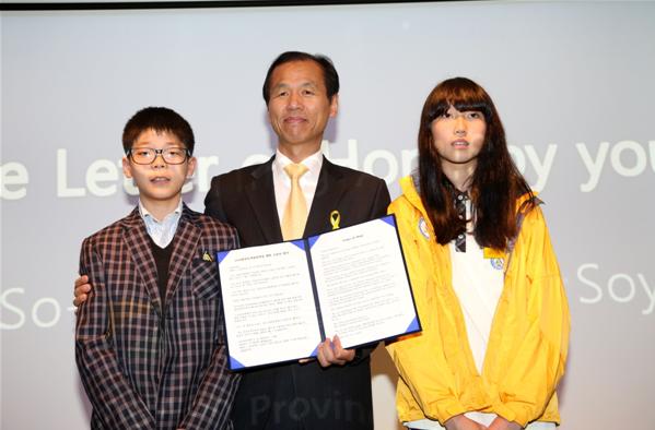 學生們在2014年4月28日召開的2018年平昌冬奧會賽場建設(shè)促進情況新聞發(fā)布會上朗讀信件，祝愿冬奧會成功舉辦。江原道知事崔文洵與學生們合影留念。